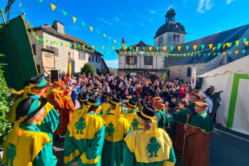 Fête de la Châtaigne à Mourjou avec confréries en costume, public rassemblé et église en arrière-plan