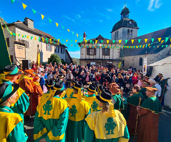 Fête de la Châtaigne à Mourjou avec confréries en costume, public rassemblé et église en arrière-plan